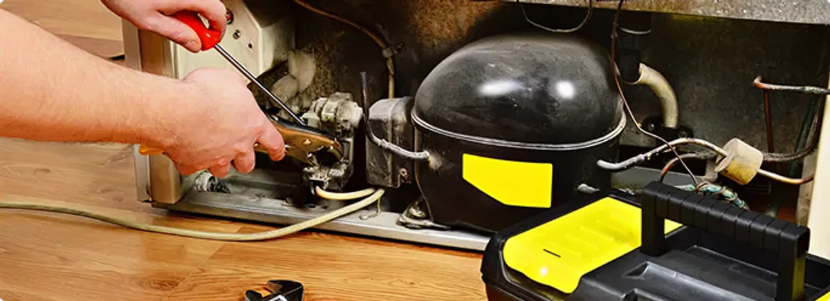 Refrigerator repair technician fixing the compressor and wiring in Fargo, ND